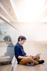 反映年轻的亚洲商人喜欢听音乐耳机，同时使用笔记本电脑在共同的工作空间。 城市工作空间概念中自由职业者或数字游牧生活方式