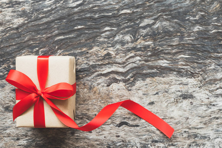 包装手工工艺纸棕色礼品盒与红色长尾丝带蝴蝶结在古老和乡村的木制背景与复制空间。 圣诞新年和生日快乐礼物的概念，老式色调。