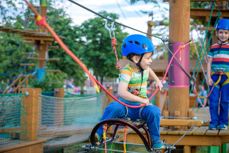 小可爱的男孩在夏天阳光明媚的日子里在攀岩冒险公园里享受活动。 蹒跚学步的孩子在绳索操场结构中攀爬。 安全攀登极限运动与头盔和卡宾