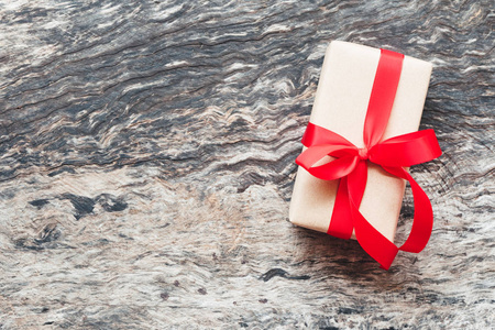 包装手工工艺纸棕色礼品盒与红色丝带弓在旧的和乡村的木制背景与复制空间。 圣诞新年和生日快乐礼物的概念，老式色调。