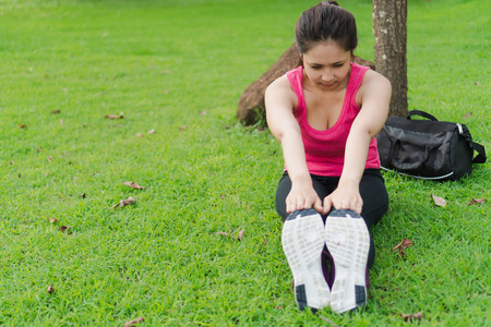 年轻的健身妇女在跑步前伸展身体，在公园户外锻炼。 漂亮的女跑步者穿着运动服，早上坐在花园里锻炼，专注于鞋子。 健康和生活方式的概