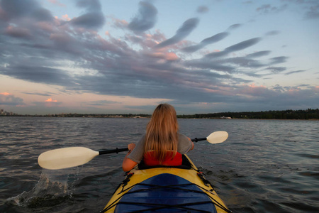 在一个充满活力的日落中,皮艇上的女人正在海洋中划船.