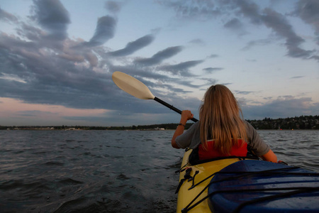 在一个充满活力的日落中，皮艇上的女人正在海洋中划船。 摄于加拿大不列颠哥伦比亚省温哥华。 概念冒险度假生活方式体育娱乐活动度假