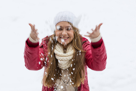 一个金发的年轻漂亮女孩喜欢第一场雪。 红色夹克，白色帽子和手套。 冬天的时候。