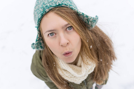 一个金发的年轻漂亮女孩喜欢第一场雪。 绿色夹克，绿色帽子和手套。 上面的风景。 复制空间。