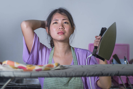 年轻漂亮的沮丧和压力亚洲的中国女人，带着熨斗在家工作，厨房熨烫衣服，绝望和不知所措在家女佣服务，家务，家务，家务压力