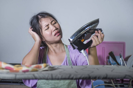 年轻的肖像，相当沮丧和压力，亚洲韩国妇女拿着熨斗在家工作，厨房熨烫衣服，绝望和不知所措在家女佣服务，家务压力