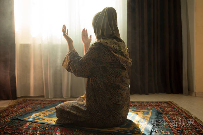 穆斯林妇女在窗户附近的房间里为真主祈祷穆斯林妇女的双手在地毯上
