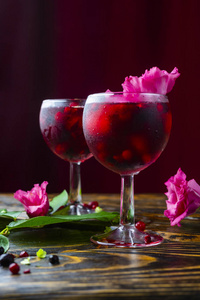 两杯装满红色饮料的浆果冰和一朵粉红色的花，旁边放着浆果和一枝绿色的热带叶子在一张老式的木桌上。 复制空间。 商业设计。