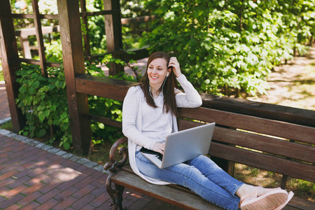 年轻成功的女商人穿着轻便的便服。 坐在长凳上工作的现代笔记本电脑电脑在城市公园的户外自然。 移动办公室。 自由职业商业概念