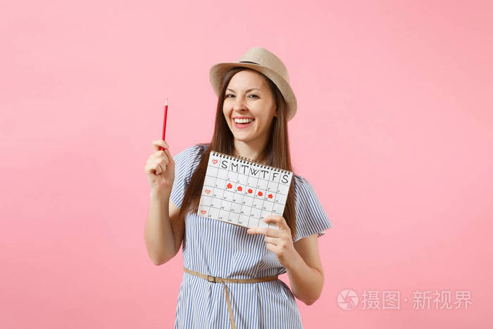 年轻女子的肖像，穿着蓝色连衣裙，戴着红色铅笔，女性月经日历，检查孤立在粉红色背景上的月经天数。 医疗保健妇科概念。 复制空间