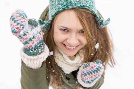 一个金发的年轻漂亮女孩喜欢第一场雪。 绿色夹克，绿色帽子和手套。 上面的风景。 复制空间。