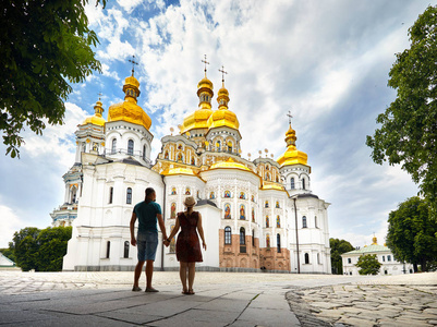 年轻的旅游夫妇在剪影中看着教堂与金色圆顶在基辅山核桃拉布拉基督教综合体。 乌克兰基辅的旧历史建筑