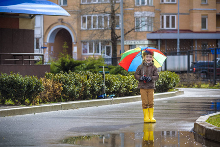 孩子穿着五颜六色的彩虹伞防水外套和靴子,在水坑里跳,在雨中跳泥.