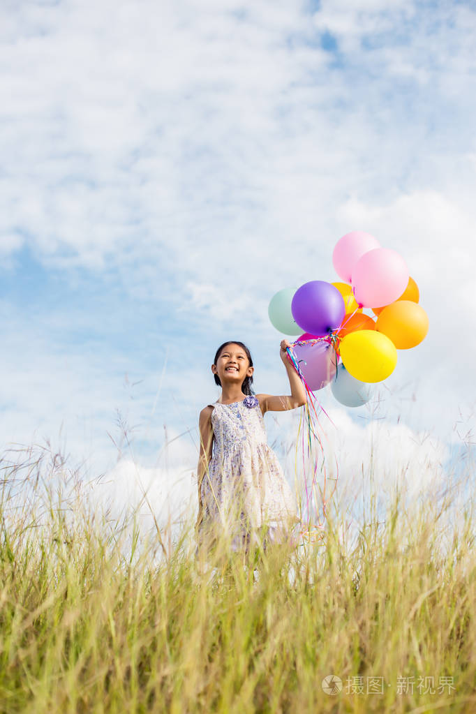 可爱的小女孩拿着五颜六色的气球在草地上对抗蓝天和云散布的手