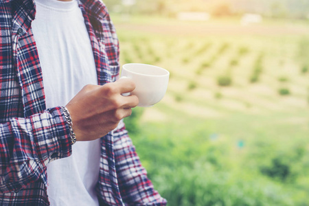 英俊的时髦胡子男人带着一杯早晨的咖啡在公园里散步。