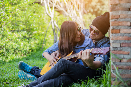 时髦的男人为他的女朋友在户外对着砖墙玩吉他。