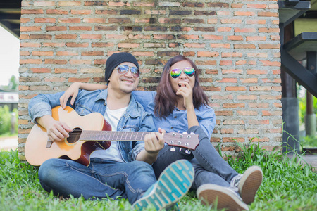 时髦的男人为他的女朋友在户外对着砖墙玩吉他。
