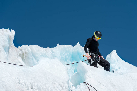 一个专业的登山运动员在头盔和滑雪面具上的保险确实在冰川上的冰斧缺口。一个职业登山者在冬季对蓝天的冰川上的工作