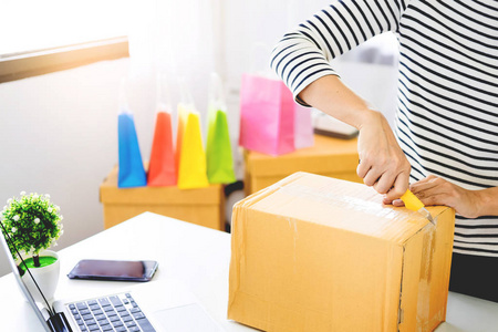 电子商务送货理念和在线销售，创业小企业主包装在卡盒在工作场所。 自由职业女卖家准备产品包装过程在商店。