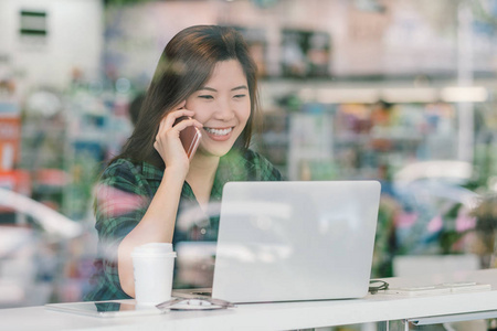 亚洲女商人的肖像，穿着休闲服，在现代办公室，企业主和企业家的概念中，在桌子旁的玻璃旁边，用科技笔记本电脑聊天和工作。