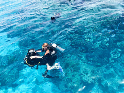 三名水下潜水员穿着黑色潜水服，一名男子和一名女子带着氧气瓶在一个热带天堂温暖的度假胜地的海洋中的透明蓝色水下下沉。