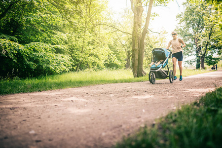 跑步的女人带着婴儿车在公园里享受夏日。 慢跑或动力步行超级运动活跃家庭与婴儿慢跑。