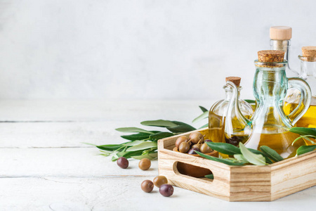 饮食和营养概念。 各种新鲜的有机特级初榨橄榄油，装在带有绿叶的瓶子里，放在乡村木桌上。 复制白色背景
