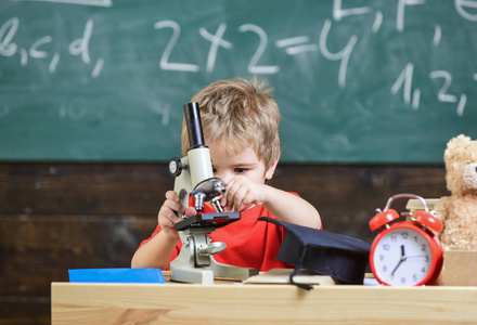 小男孩在教室里工作, 黑板上的背景。孩子在繁忙的面孔附近时钟和泰迪熊。小学的概念。第一个对学习, 学习, 教育感兴趣的前