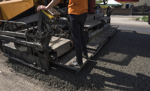 工人操作沥青摊铺机在道路施工和维修工程。摊铺机的精轧机沥青精轧机或铺有一层沥青的铺路机械。加铺改建