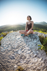 日落时，一个女孩坐在山顶上。 一个女人从事瑜伽。 冥想离文明很远。 对美丽自然的沉思。 山的景色。