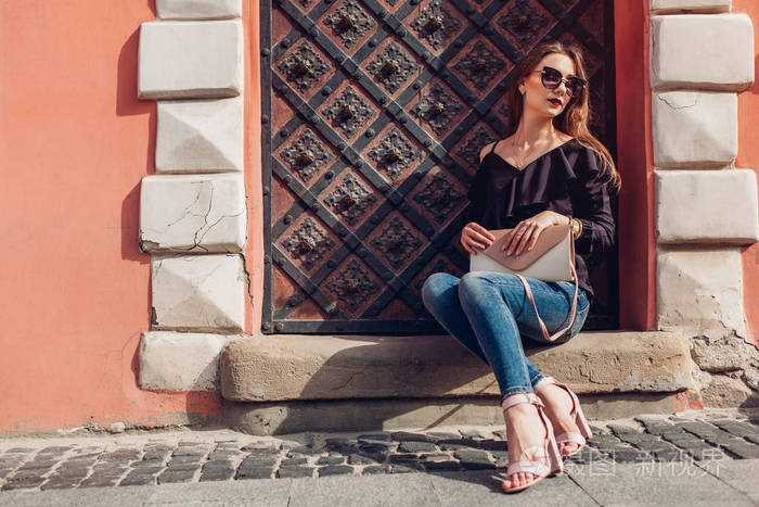 一位戴太阳镜的漂亮时尚女人坐在城市街道上的户外肖像.