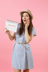年轻女子的肖像，戴着蓝色连衣裙帽子，日历，检查月经天数，孤立在明亮的趋势粉红色背景上。 医疗保健妇科概念。 复制空间