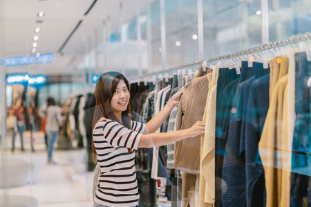 快乐的亚洲女人在百货商店里挑选衣服，在百货公司中心快乐地活动