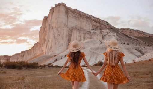 年轻的女人穿着裙子，在日落时在白岩边玩。 漂亮的两对双胞胎穿着时尚的衣服。 农村农场女孩生活方式户外肖像。 模特戴着时尚的草帽。