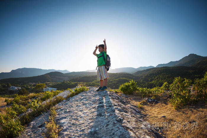 山顶上的一个男孩一个带背包的孩子正在旅行山和美丽的天空背景上的