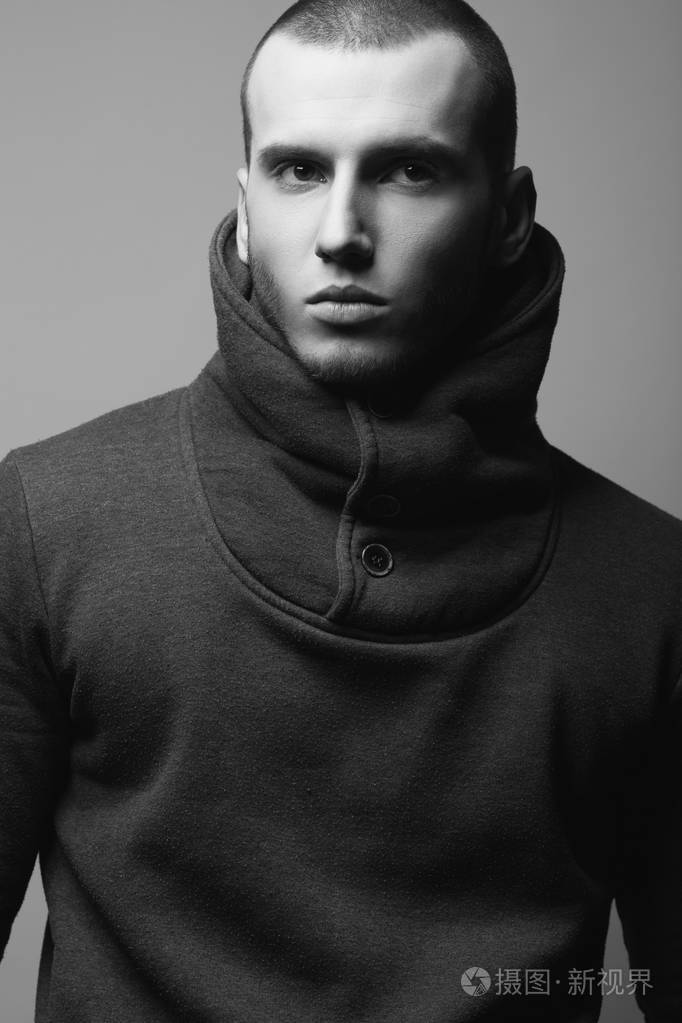 残酷的年轻人的肖像,短发,穿灰色运动衫,高领,在灰色背景上摆姿势.