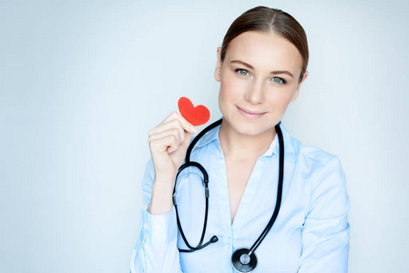 一位手握小红心脏的女医生的肖像，被隔离在蓝色清晰的背景心脏病学诊所概念照片上