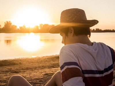 日落时坐在沙滩上戴夏帽的少年的后景