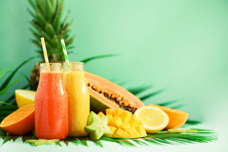多汁木瓜和菠萝, 芒果, 橙果冰沙在两个罐子上绿松石背景。排毒, 夏季减肥食品, 素食主义的概念。复制空间。绿棕榈叶玻璃瓶中的鲜