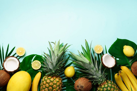 异国情调的菠萝, 成熟的椰子, 香蕉, 瓜, 柠檬, 热带棕榈和绿色龟背竹叶子在蓝色背景与 copyspace 为您的文本。创意