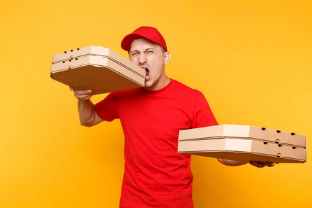 送货员穿着红色帽子T恤，在黄色背景上隔离了食品订单披萨盒。 男员工皮萨曼或快递员制服持有意大利披萨在纸板平板盒。 服务概念