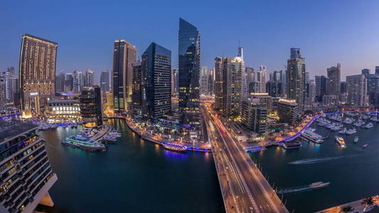 美丽的鸟瞰白天到夜间过渡时间，所有迪拜码头长廊和运河与浮动游艇和船只后，迪拜阿联酋。 桥上的现代塔楼和交通。