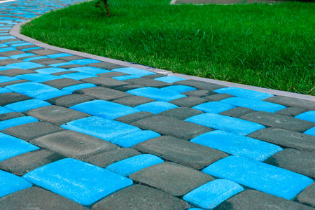 一条从明亮的蓝色瓷砖铺在多汁的绿色草坪附近的小径。 明亮的熟料瓷砖不同颜色的家。 用于瓷砖目录中的广告瓷砖制造商。