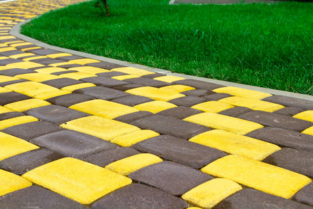 从一条明亮的黄色瓷砖铺在多汁的绿色草坪附近的小径。 明亮的熟料瓷砖不同颜色的家。 用于瓷砖目录中的广告瓷砖制造商。