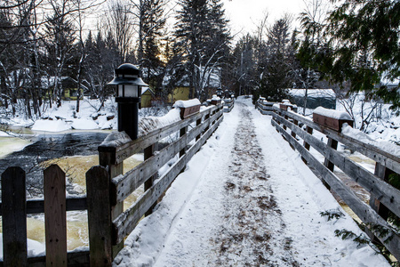有灯笼和白雪覆盖的木板箱的人行桥穿过一条部分湍急的河流