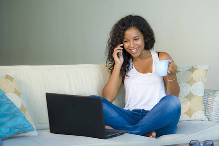 生活方式孤立的照片年轻，快乐和美丽的黑人非洲裔美国妇女在家中使用笔记本电脑沙发沙发上工作时用手机说话