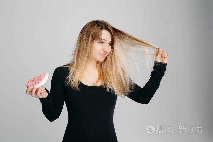漂亮的女人拿着凌乱的头发在一只手和梳子在另一只
