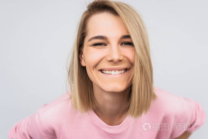 特写肖像正面美丽的微笑金发女性与迷人的外观穿着粉红色毛衣摆在白色