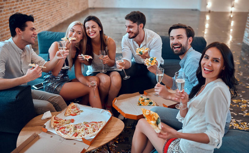 让聚会开始吧 一群年轻人在一起玩得很开心。 坐在有香槟和披萨的大光房里。 在亲密朋友的大公司庆祝节日。